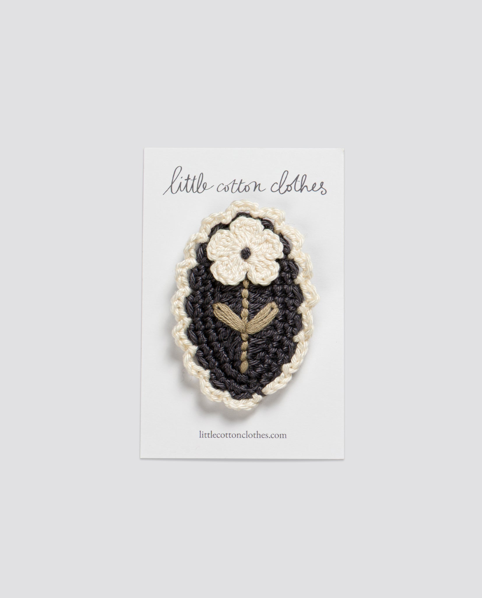 Crochet hair clip featuring a vintage-style cream flower with green stem on a navy blue oval background, ethically made for children by a slow, natural clothing brand.