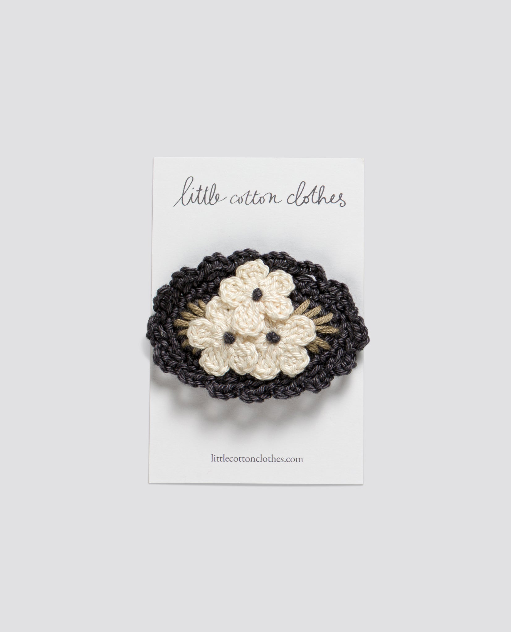 Crocheted hair clip with three delicate cream flowers on a natural dark oval base, designed for kids with a vintage, slow, and ethical style.
