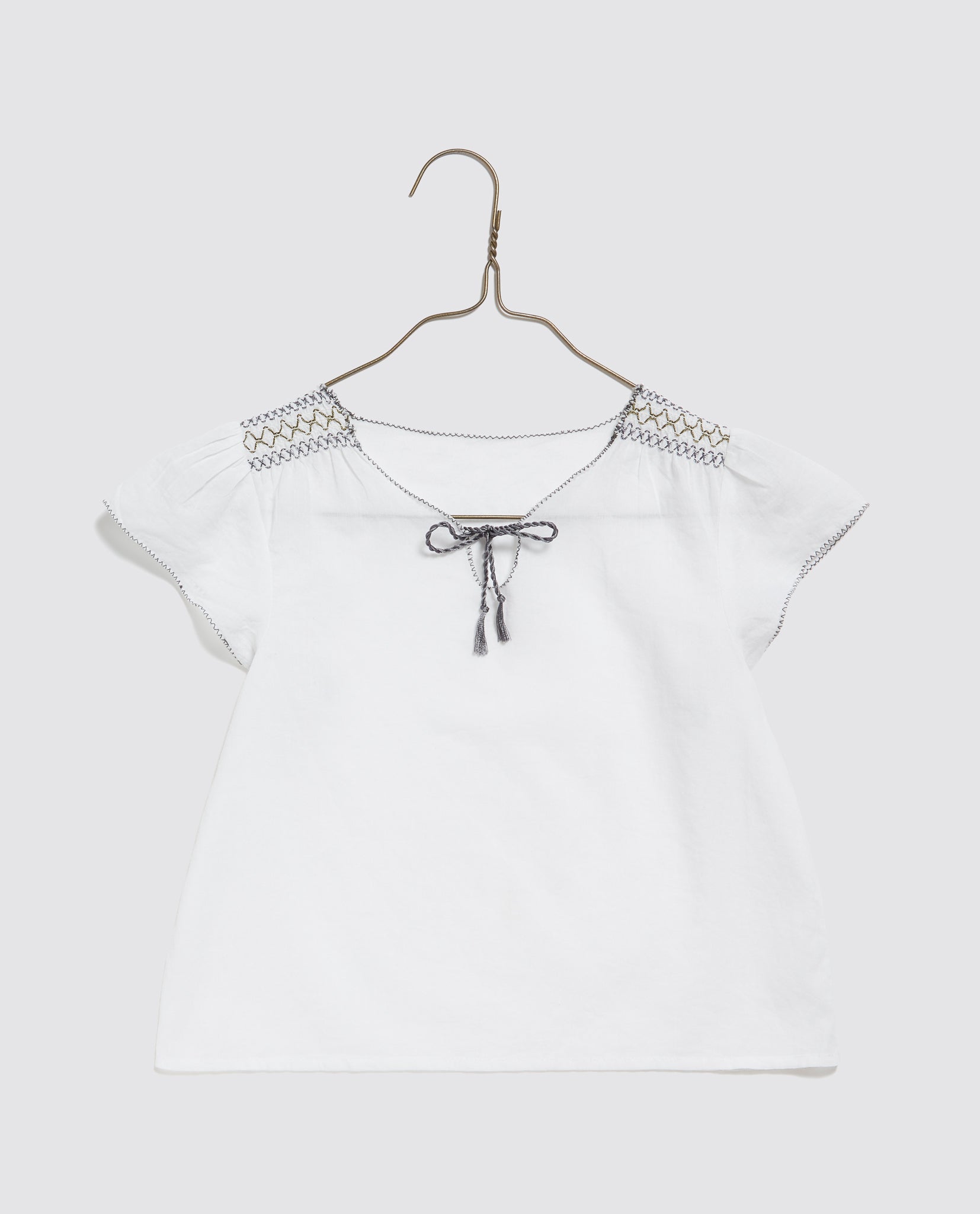 Off-white organic cotton blouse for girls with delicate vintage-inspired embroidery and a small tie at the neckline, crafted from natural sustainable materials.