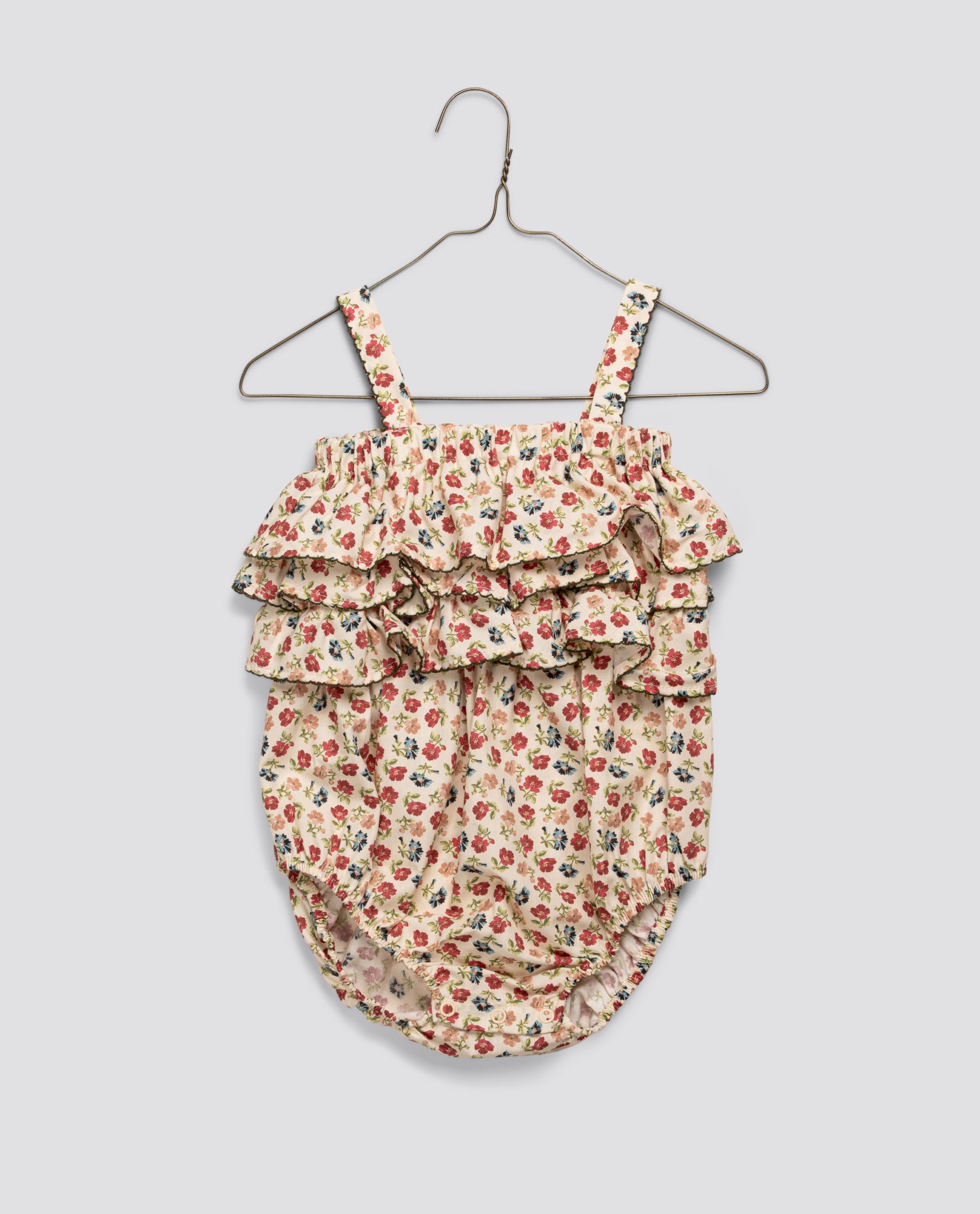 Vintage style girls romper in floral pattern, made from soft organic cotton with ruffled layers, reflecting a slow, natural, and ethical children's clothing brand.