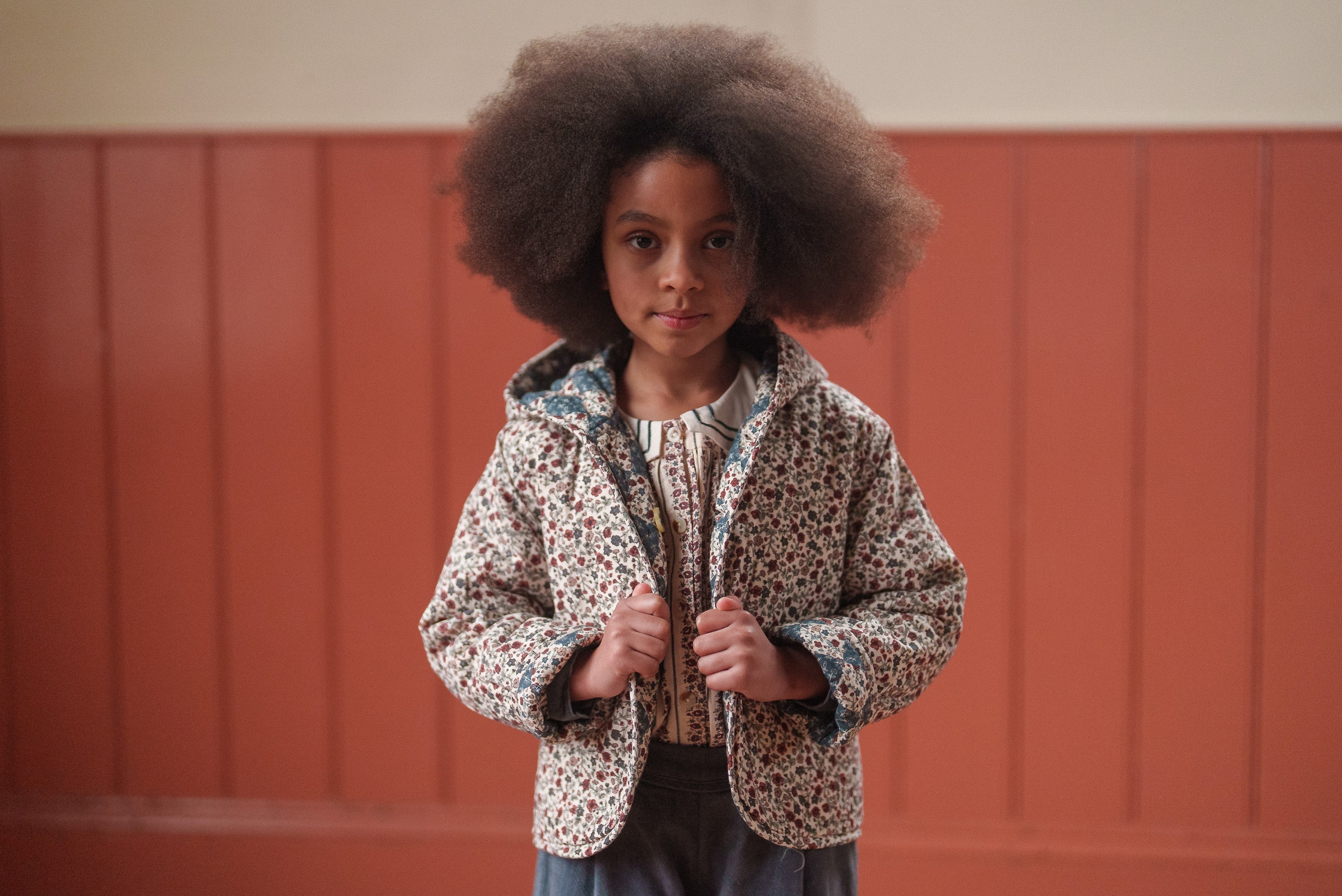Young girl wearing an organic cotton floral blouse under a quilted jacket, showcasing vintage style children's clothing made with natural, sustainable materials.