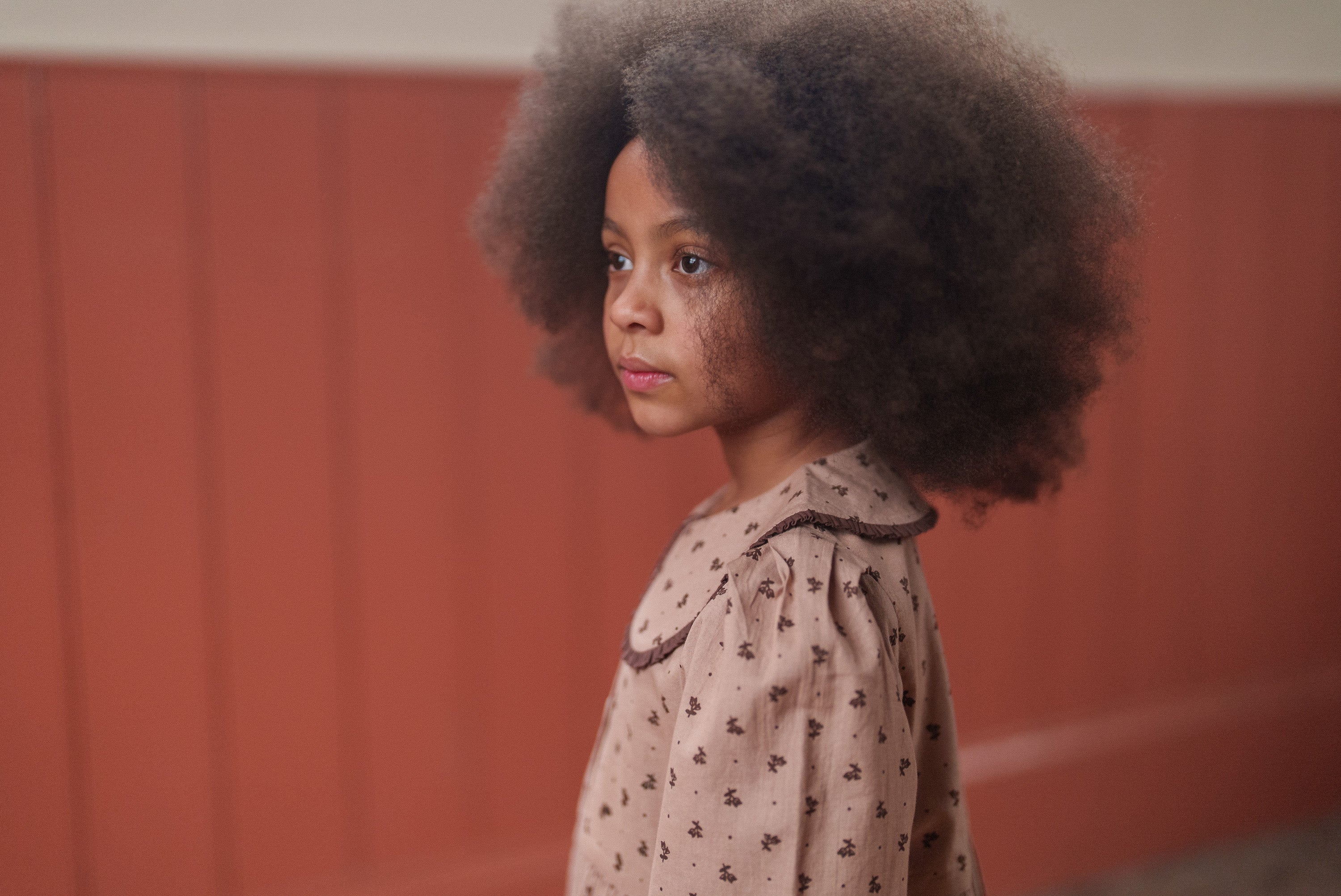 Young girl wearing a vintage-style organic cotton dress with a delicate rosehip floral pattern in soft pink and brown hues, reflecting ethical and sustainable kids clothing.