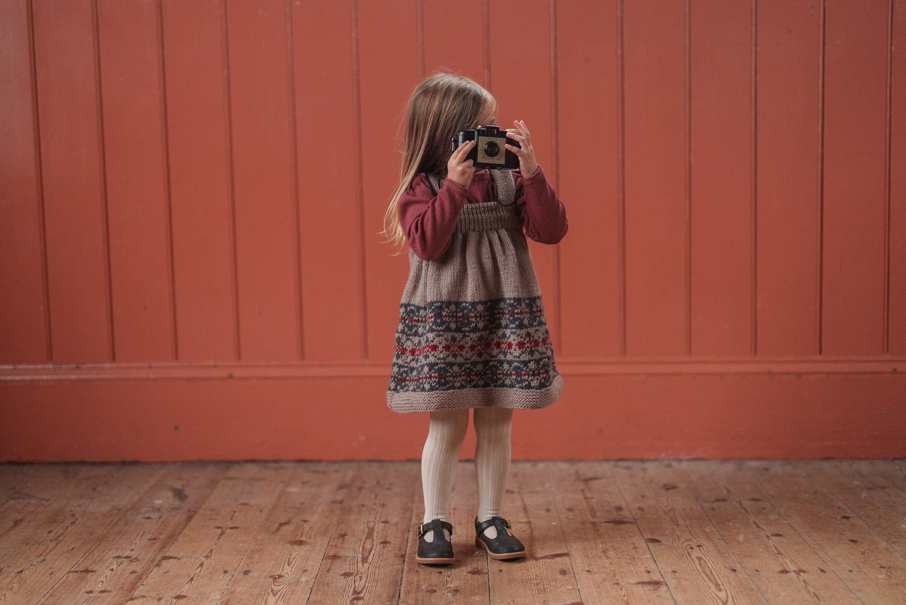 Child wearing hand-knitted pinafore dress with Fair Isle pattern in navy, blue, beige, layered over a long-sleeve top, styled in vintage sustainable children’s clothing.