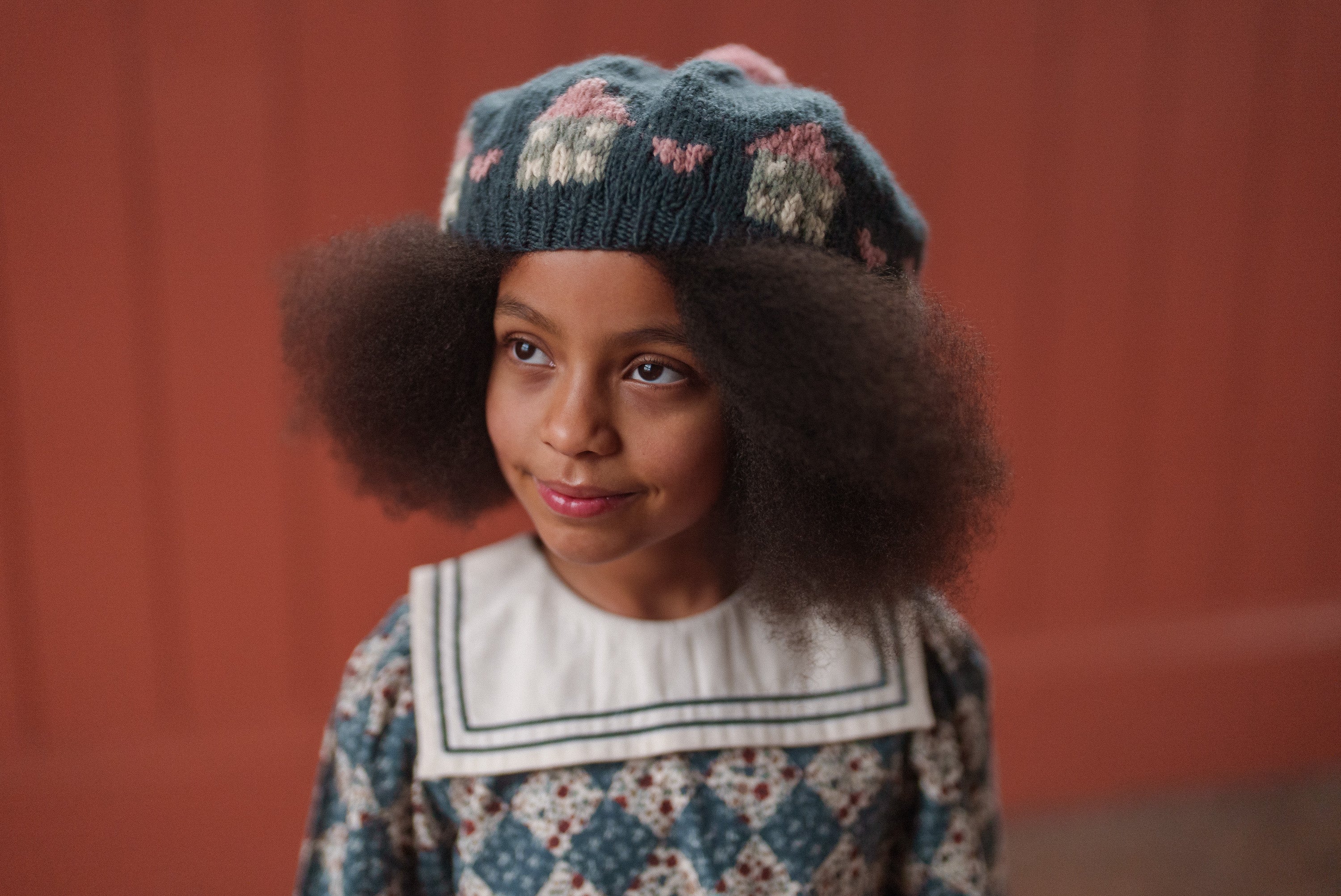 Young girl wearing a vintage style navy floral dress and matching knitted hat made from organic cotton, showcasing ethically made sustainable kids clothing.