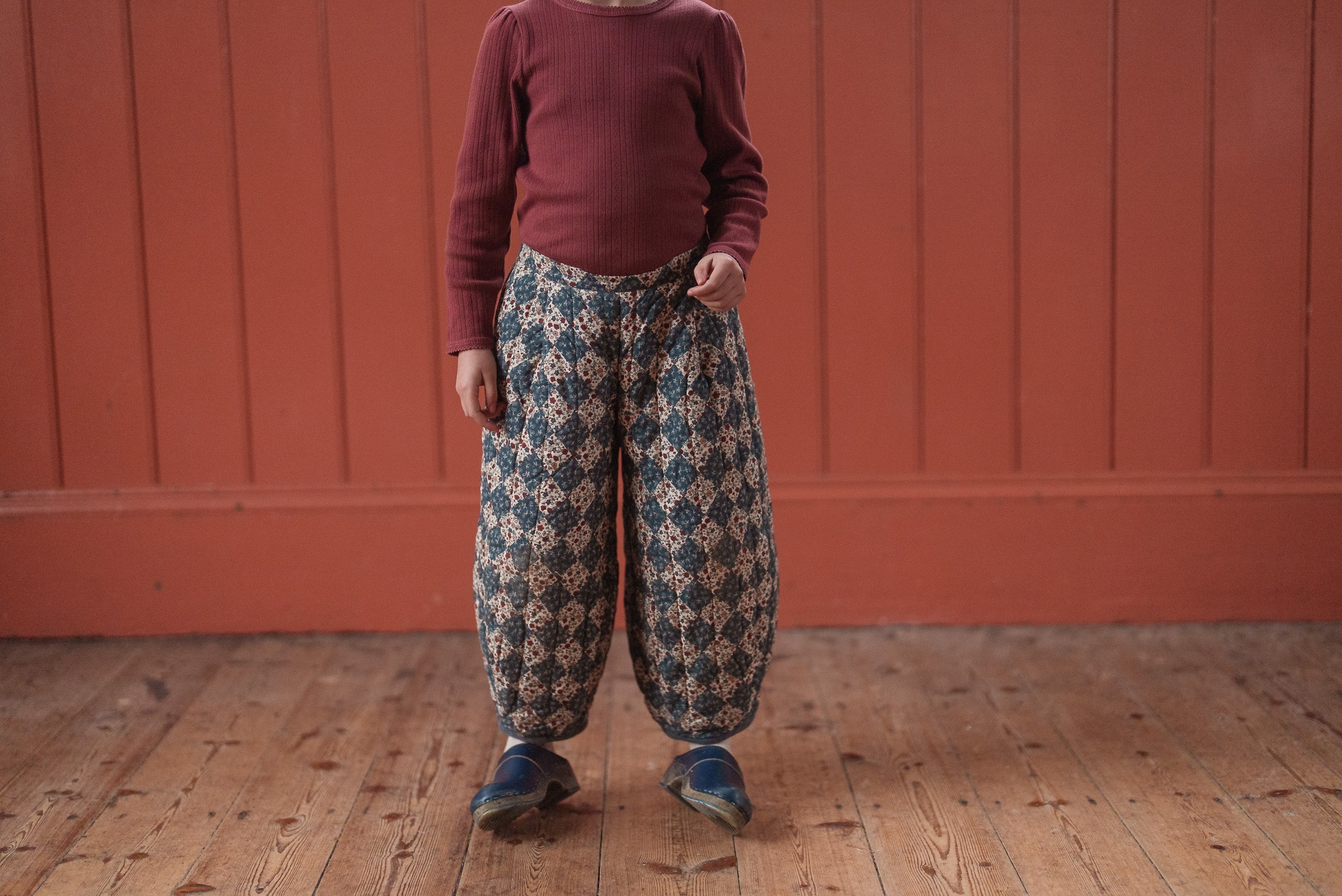 Child wearing vintage style quilted trousers with harlequin floral pattern, made from organic materials, showcasing sustainable, ethically made children’s clothing.
