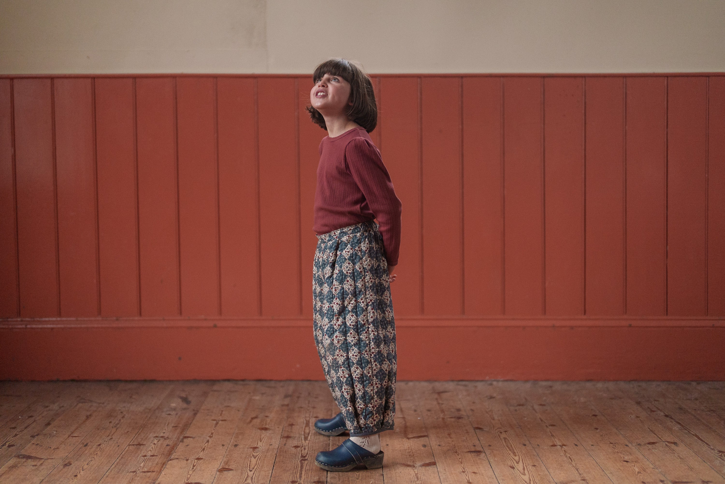 Child wearing a red organic cotton pointelle T-shirt paired with vintage-style patterned trousers in a warm, natural setting, showcasing sustainable children's clothing.