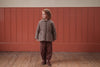 Child wearing a floral brown jacket and pants standing against a red paneled wall.