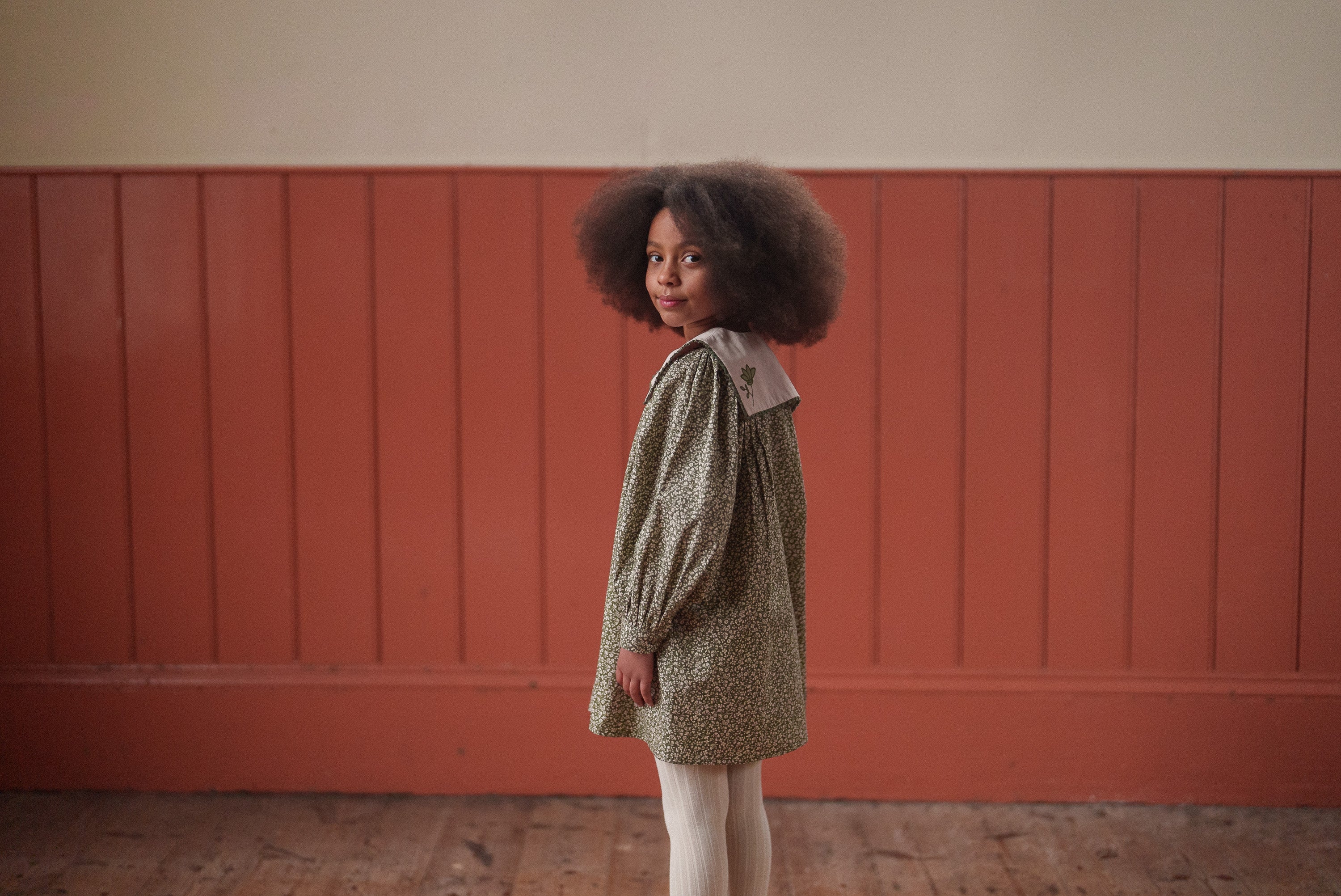 Young girl wearing a vintage-inspired green floral dress made from organic cotton, styled for a sustainable and natural look in children's clothing.
