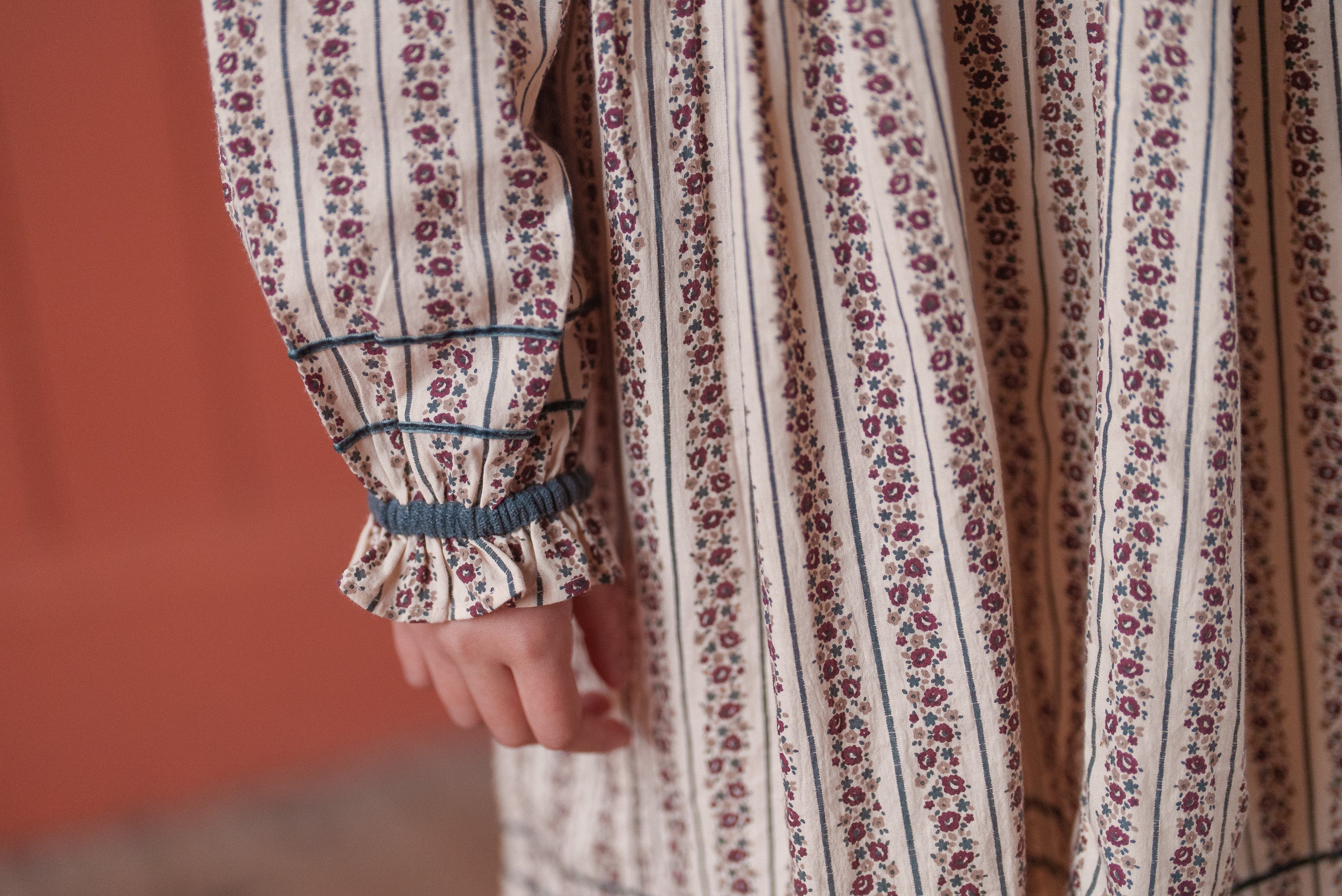 Close-up of a girl's sleeve featuring vintage style smocked details in organic cotton fabric with a delicate floral stripe pattern from a sustainable children's clothing brand.