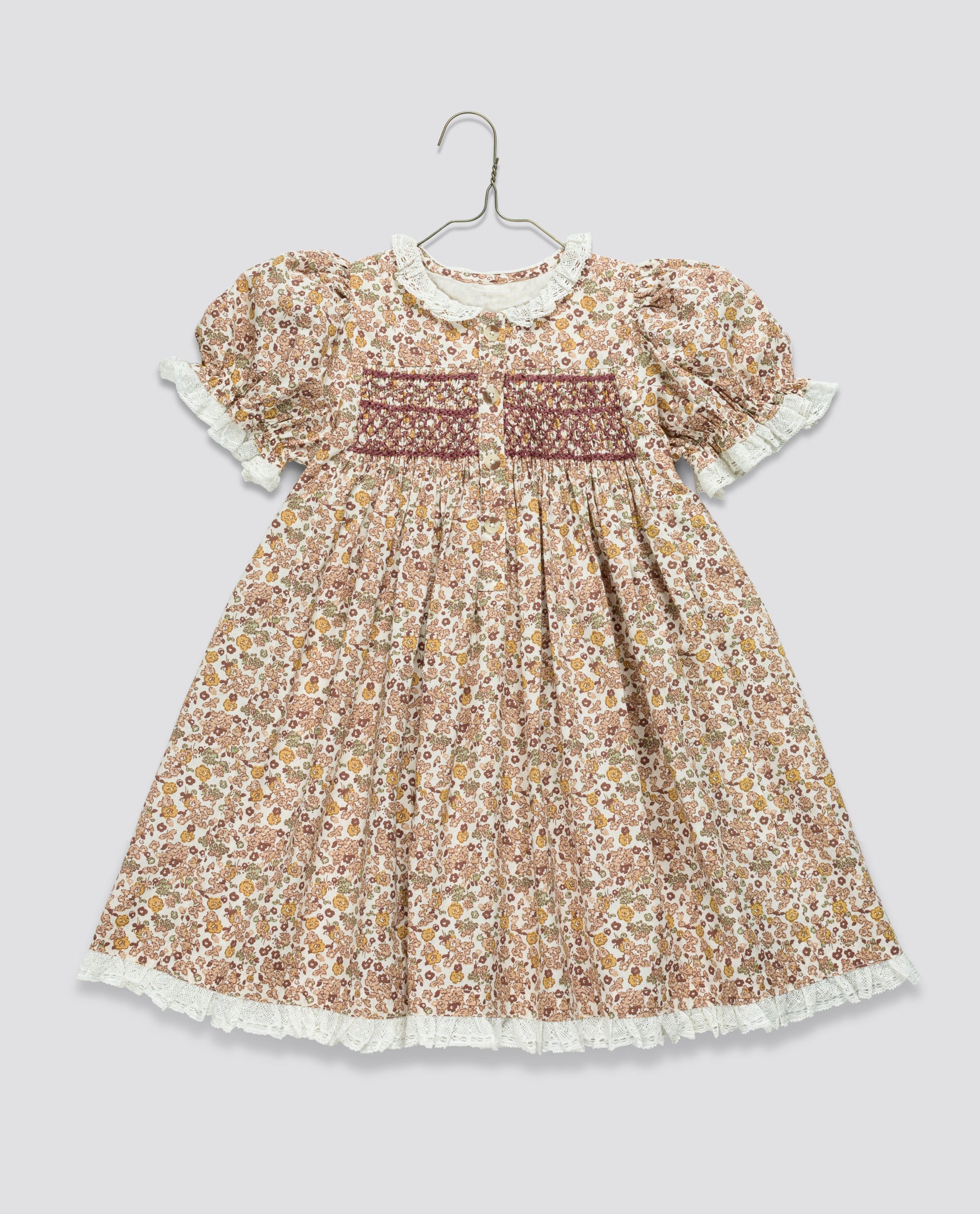 Vintage-style girls dress in a floral cotton blend with puff sleeves, lace trim, and smocked detailing, made from sustainable and organic materials.