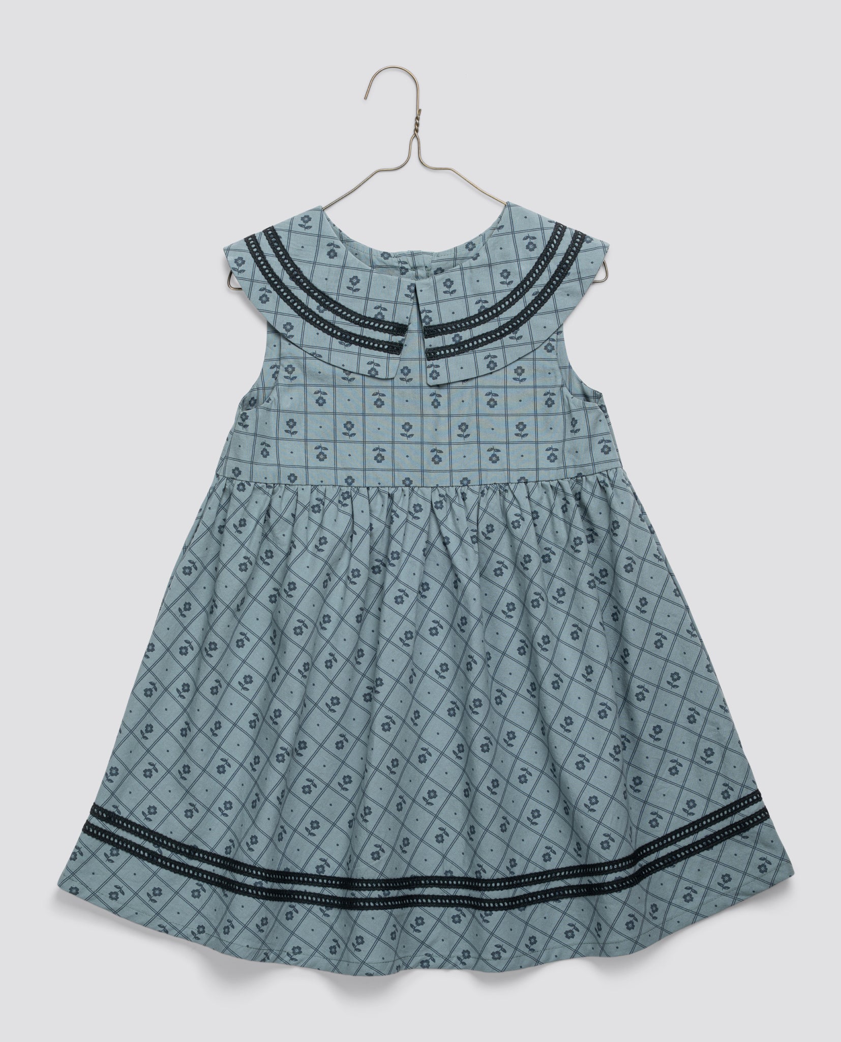 Blue vintage-style girls dress in organic cotton with thyme floral pattern, featuring a pleated bodice and decorative trim, designed with care for sustainable children's clothing.