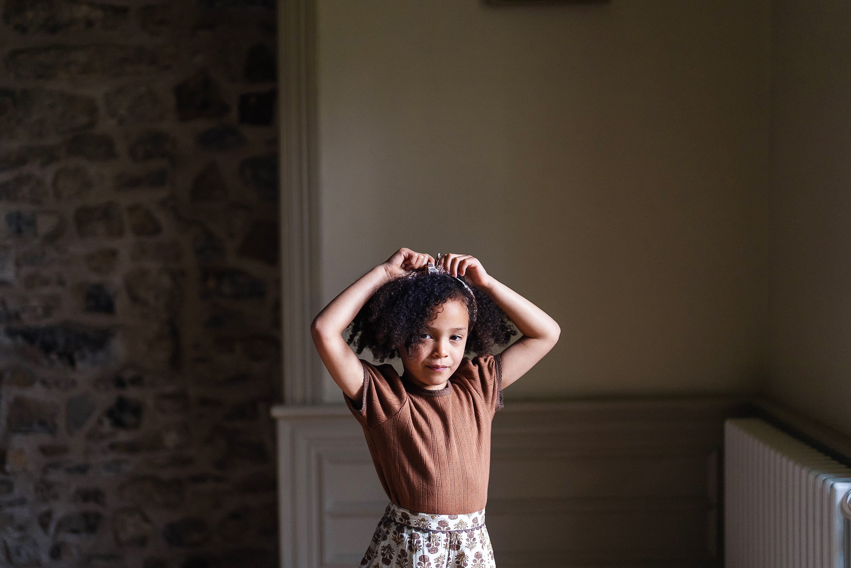 Young child wearing a cinnamon-colored organic cotton t-shirt with a vintage-inspired skirt, standing indoors in soft natural light.
