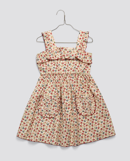 Girls vintage-style dress in organic cotton with a floral pattern, featuring ruffled straps and front pockets, designed with slow, natural, and ethical values.