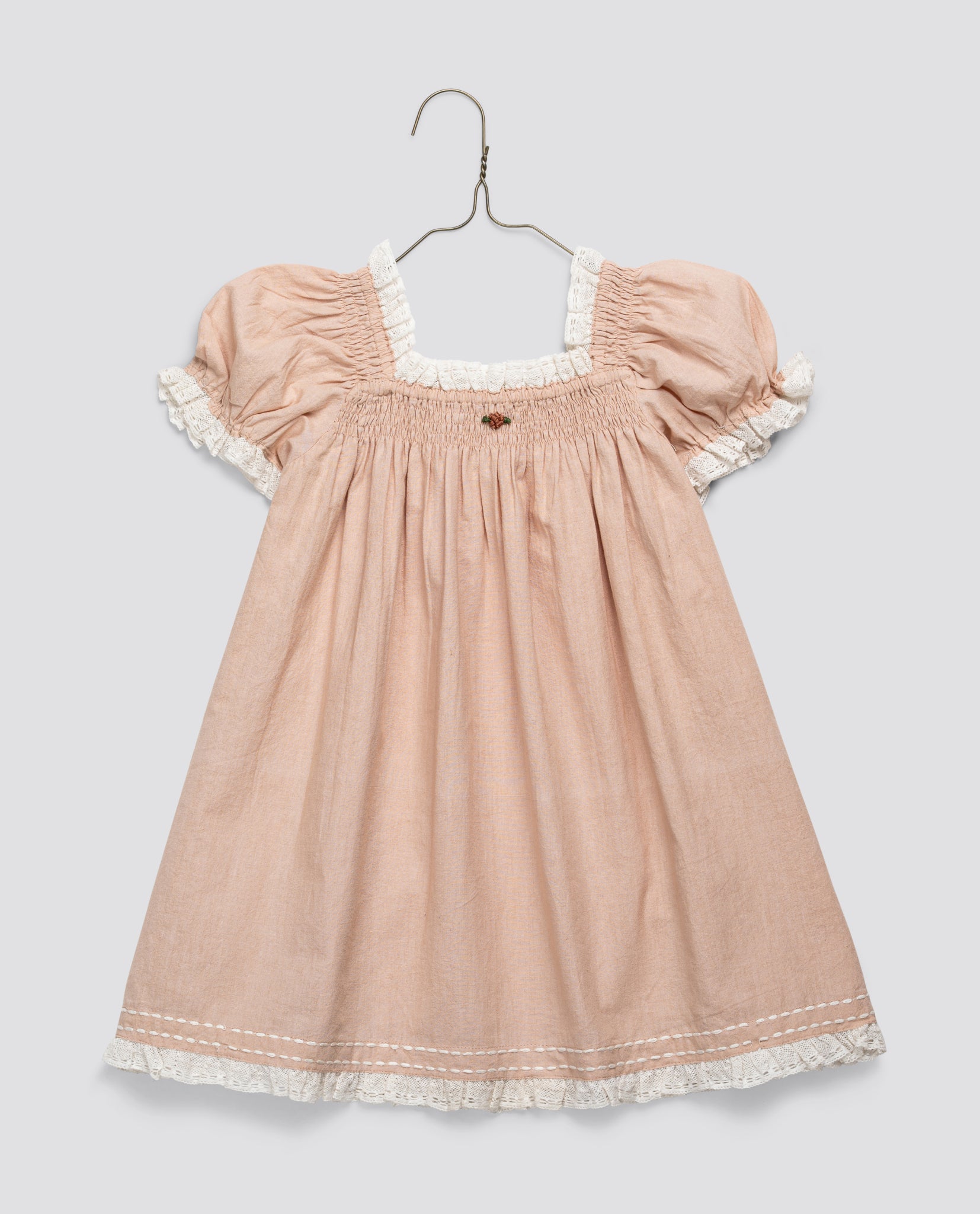 Vintage style girls dress in soft pink organic cotton with puff sleeves and delicate white lace trim, designed with traditional smocking for a timeless look.