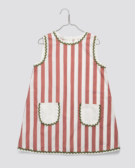 Pink and white striped vintage-style girls dress with scalloped green trim and two front pockets, made from organic cotton in an ethically made children’s clothing brand.