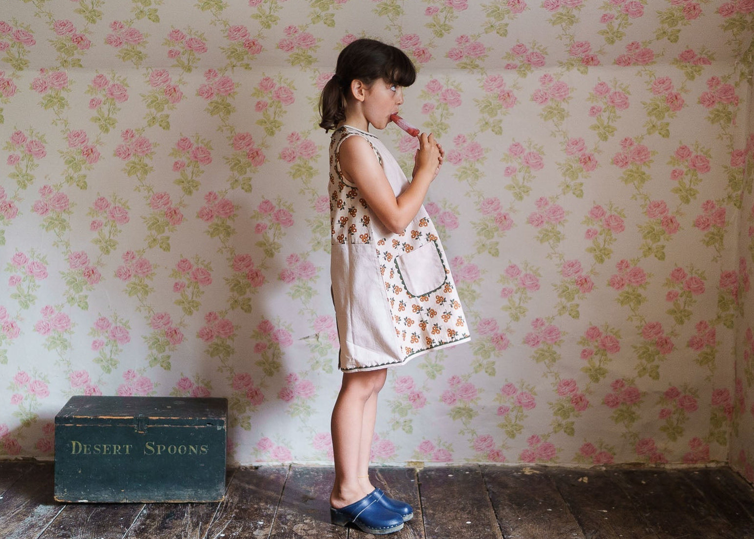 Young girl wearing a vintage-style floral organic cotton dress in a softly patterned room, embodying natural and sustainable children's clothing.