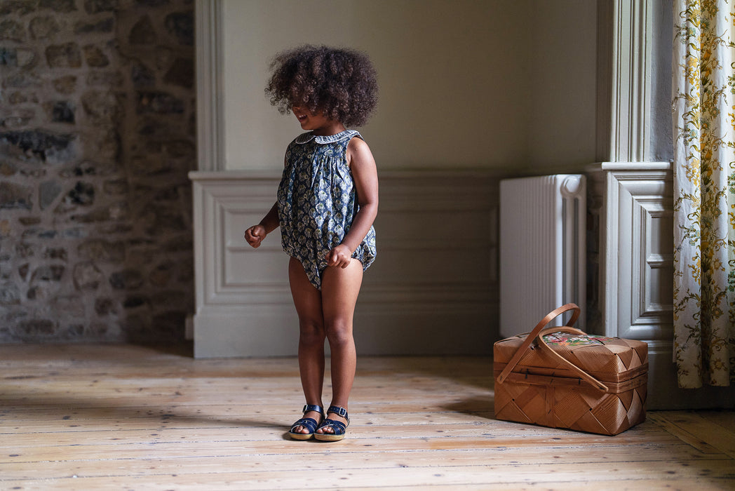 A beautiful, blue floral baby girl's bubble romper made in floral fabric with a checked peter pan collar. Elasticated leg openings and poppers. Made in a vintage inspired style.