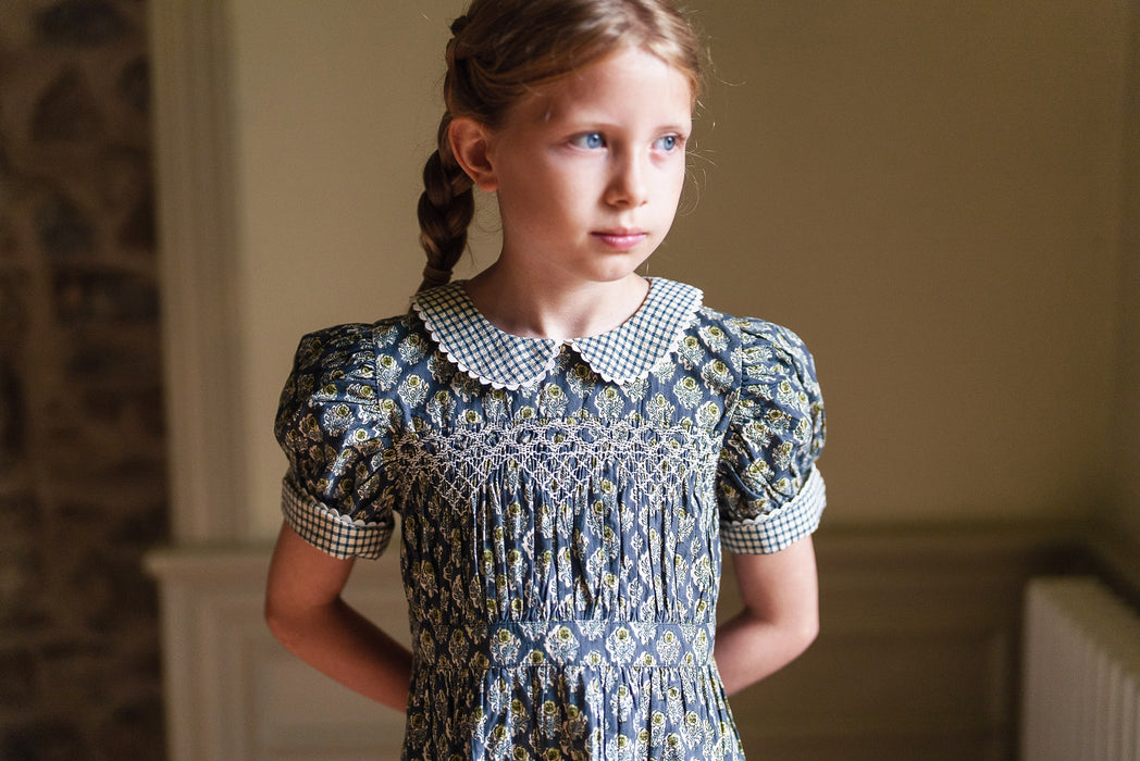 Our timeless, vintage inspired Orla Dress has been made in our organic cotton thistle floral fabric. This pretty children's dress is perfect for special occasions or everyday wear. It has beautiful hand smocking over a gathered bodice, full, puffed sleeves with contrasting cuffs and a contrasting gingham Peter Pan collar. Designed for comfort and style, the full skirt allows for easy movement, it's sure to become a favourite for little girls.  
