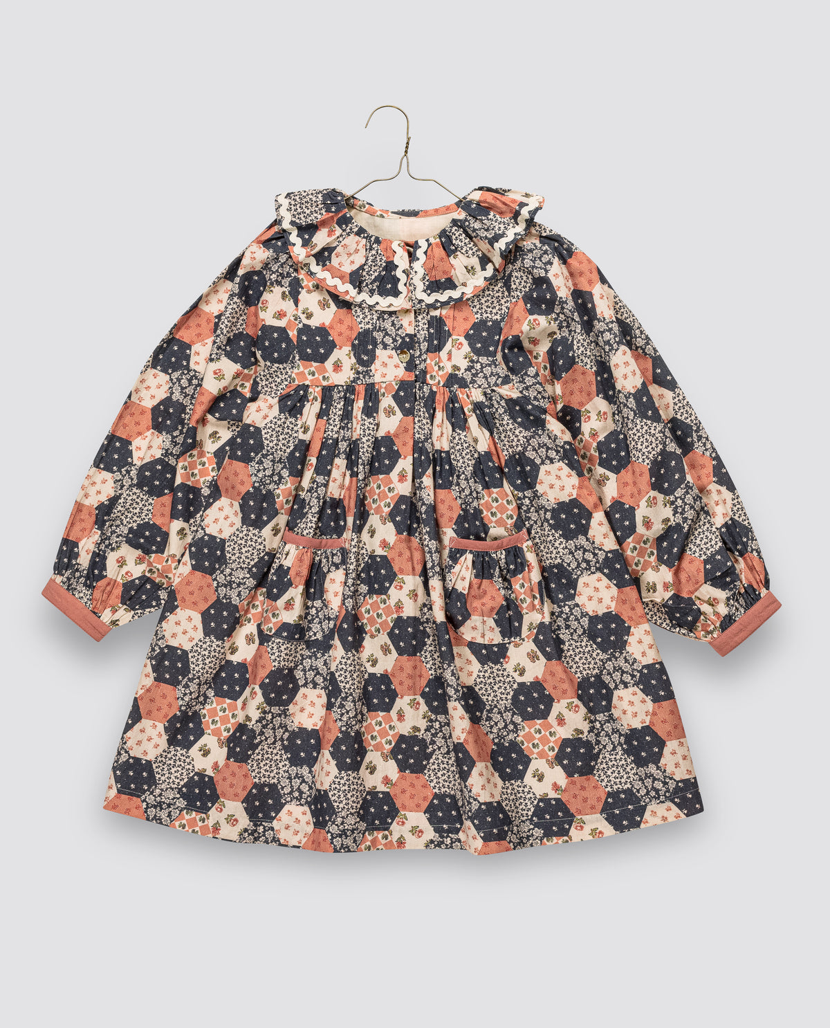 Girl's vintage-style dress in geometric patchwork with frilly collar and pockets, made from organic cotton blend for sustainable children's clothing.