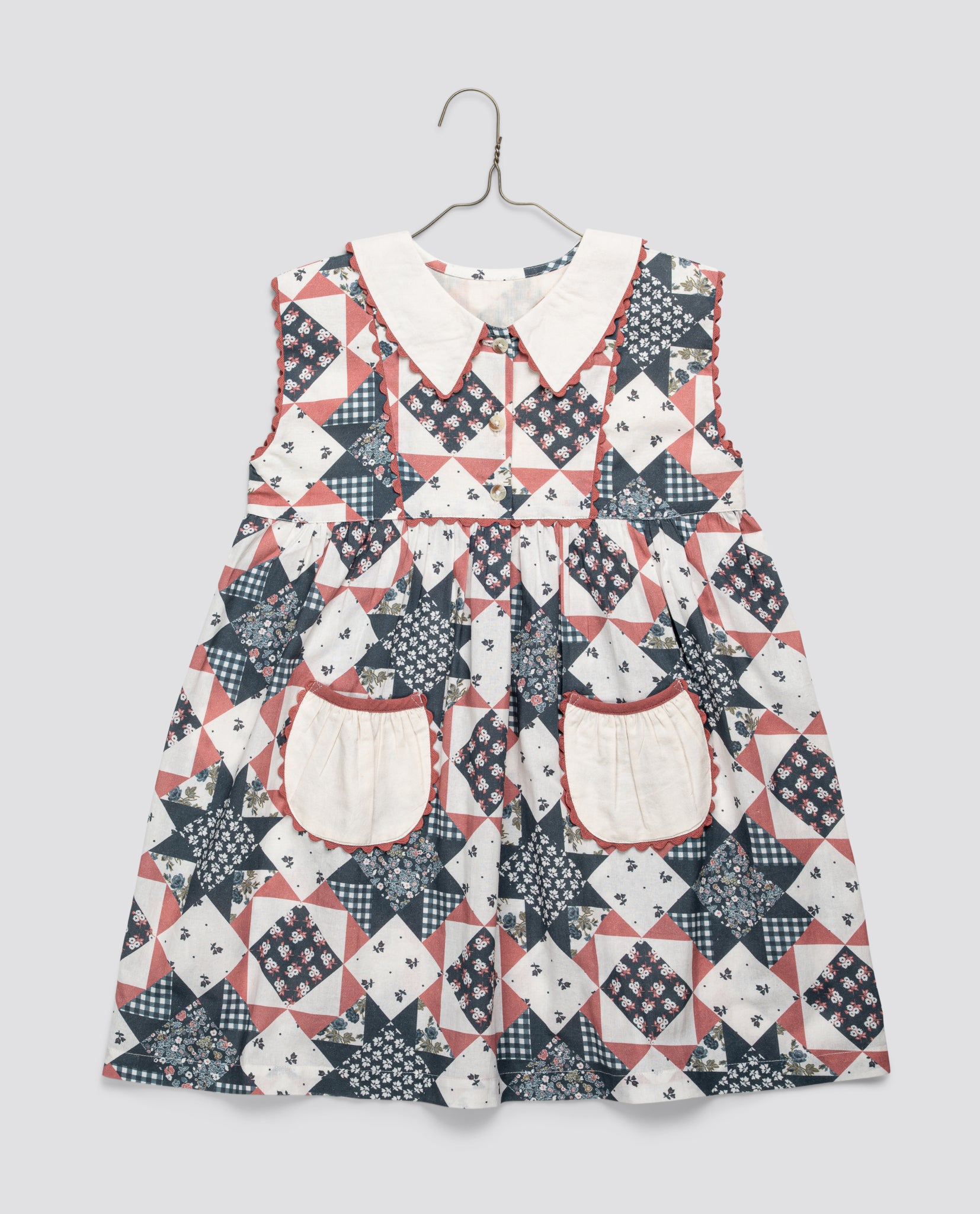 Girls vintage-style dress in blue and floral geometric patchwork with a white collar and pockets, made from organic cotton blend for sustainable kids clothing.