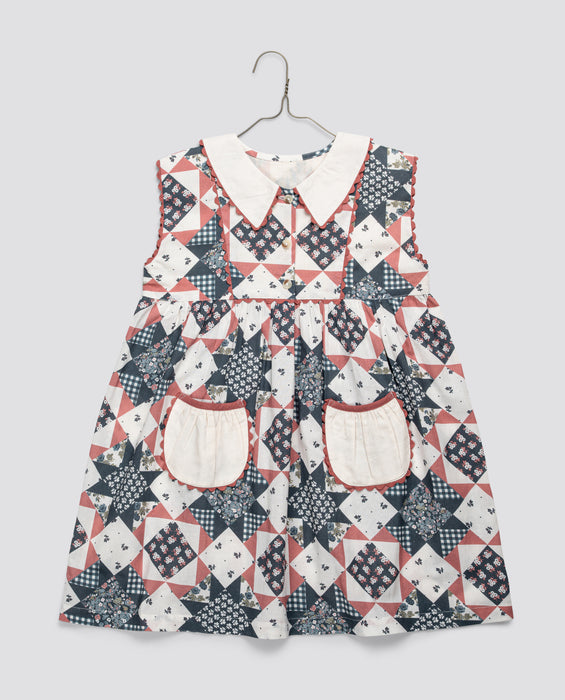 Girls vintage-style dress in blue and floral geometric patchwork with a white collar and pockets, made from organic cotton blend for sustainable kids clothing.