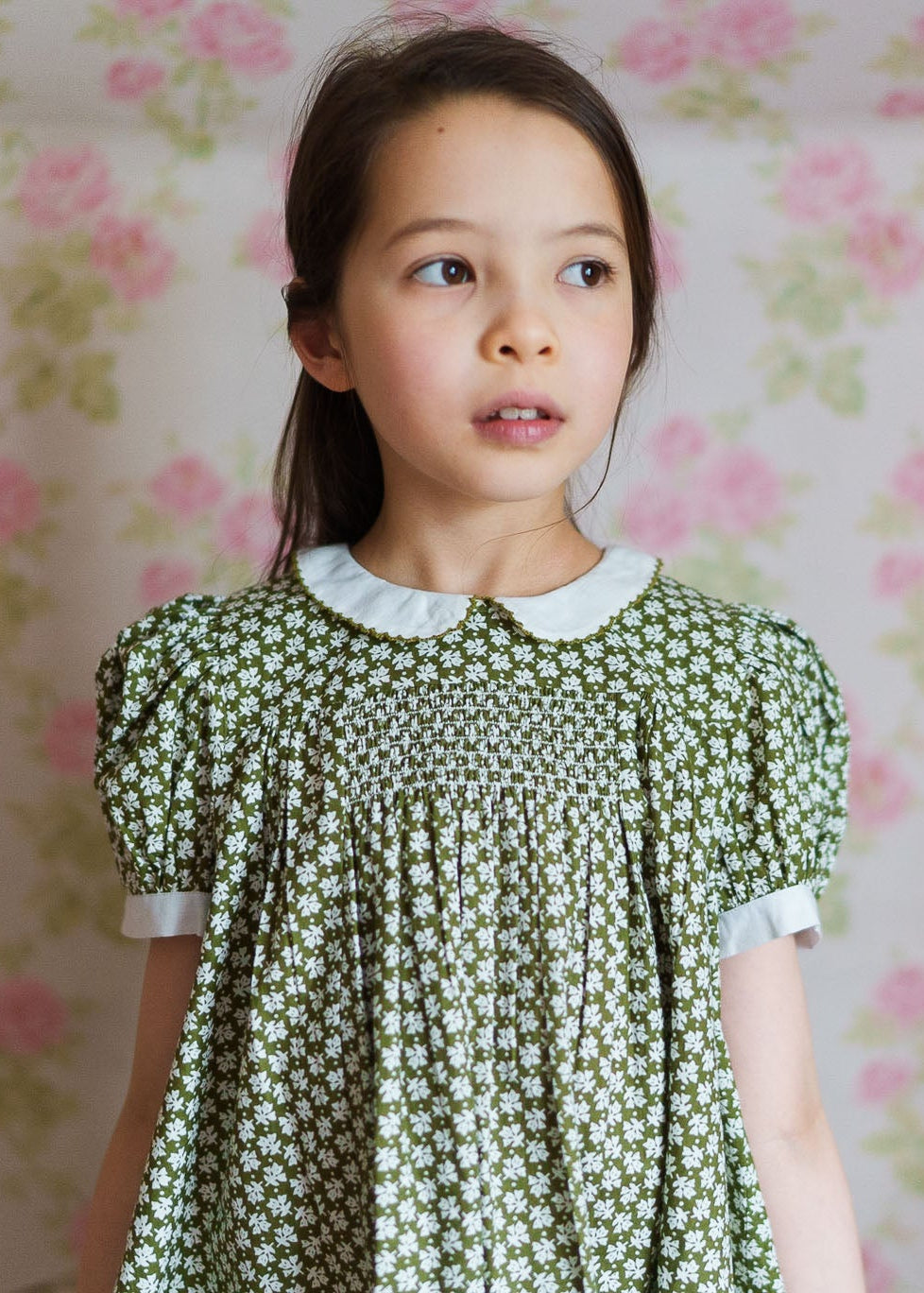 Young girl wearing a vintage style green floral cotton blend dress with a white collar, showcasing sustainable, ethically made children's clothing for toddlers and kids.