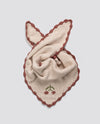 Soft cream cotton scarf with hand-knitted cherry detail and vintage-inspired rust-colored scalloped edges, crafted sustainably for children’s organic clothing.