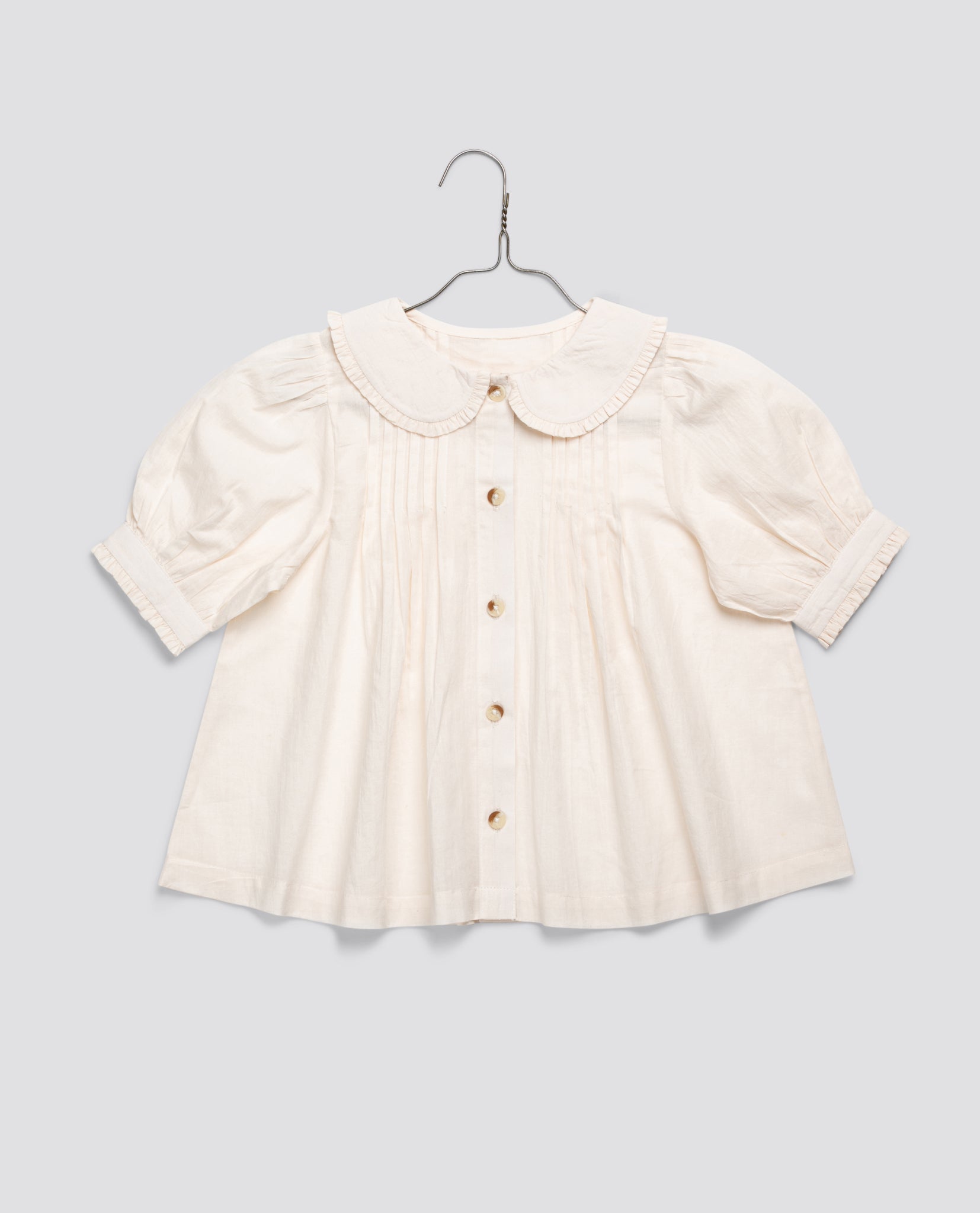 Cream-colored vintage style girls blouse made from organic cotton with puff sleeves and a delicate Peter Pan collar, reflecting natural and sustainable children's clothing.