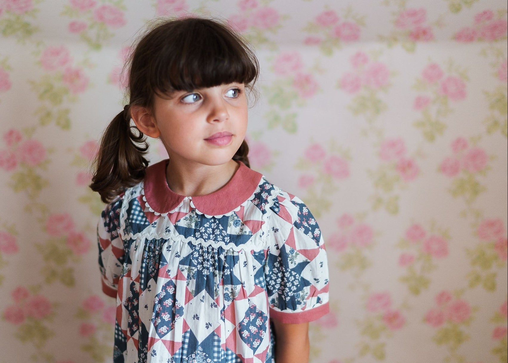 Young girl wearing a vintage style girls blouse with a soft patchwork floral pattern in gentle colors, made from organic cotton in an ethically made children’s clothing brand.