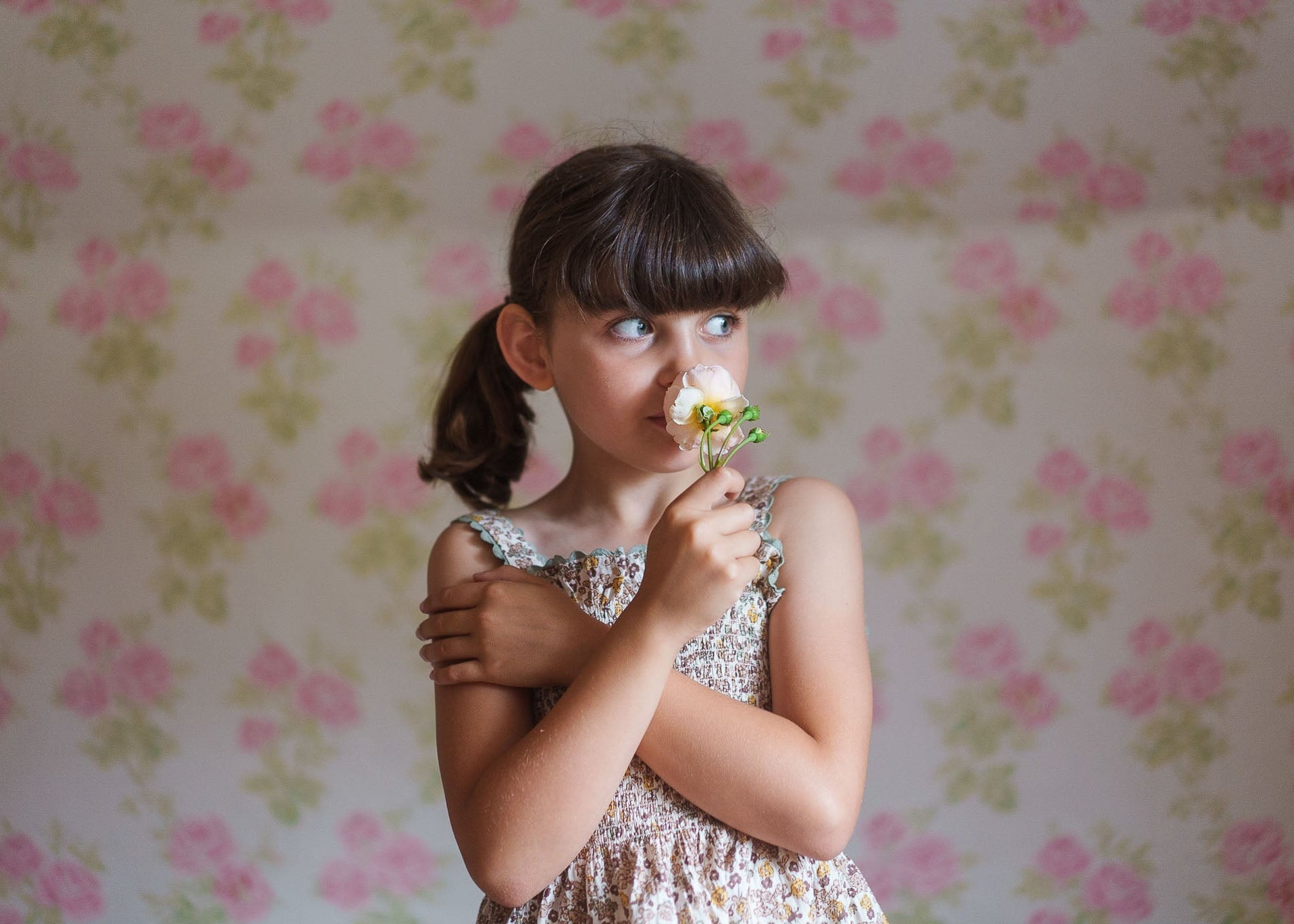Young girl in vintage-style floral dress holding a flower, showcasing sustainable, organic children's clothing made from natural materials with a soft, warm background.