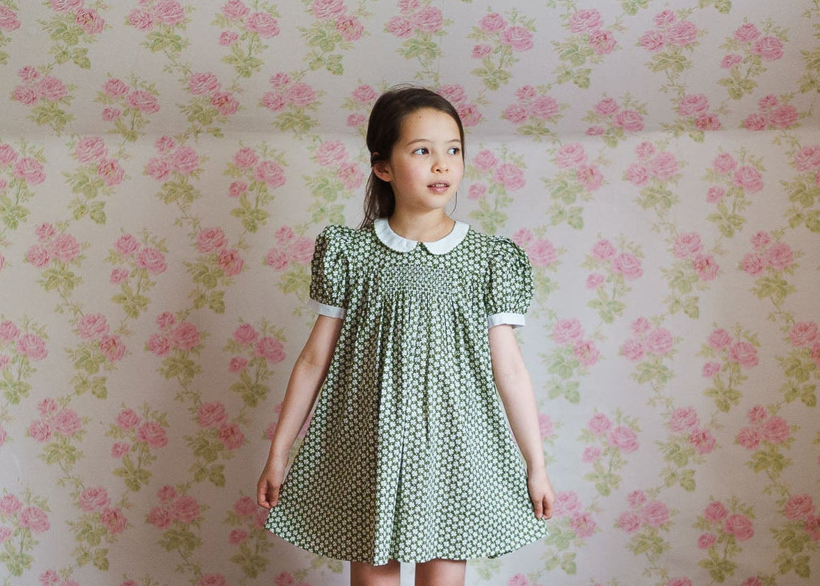 Young girl wearing a vintage-inspired green floral dress made from a soft cotton blend, reflecting ethical and sustainable children's clothing with a classic style.