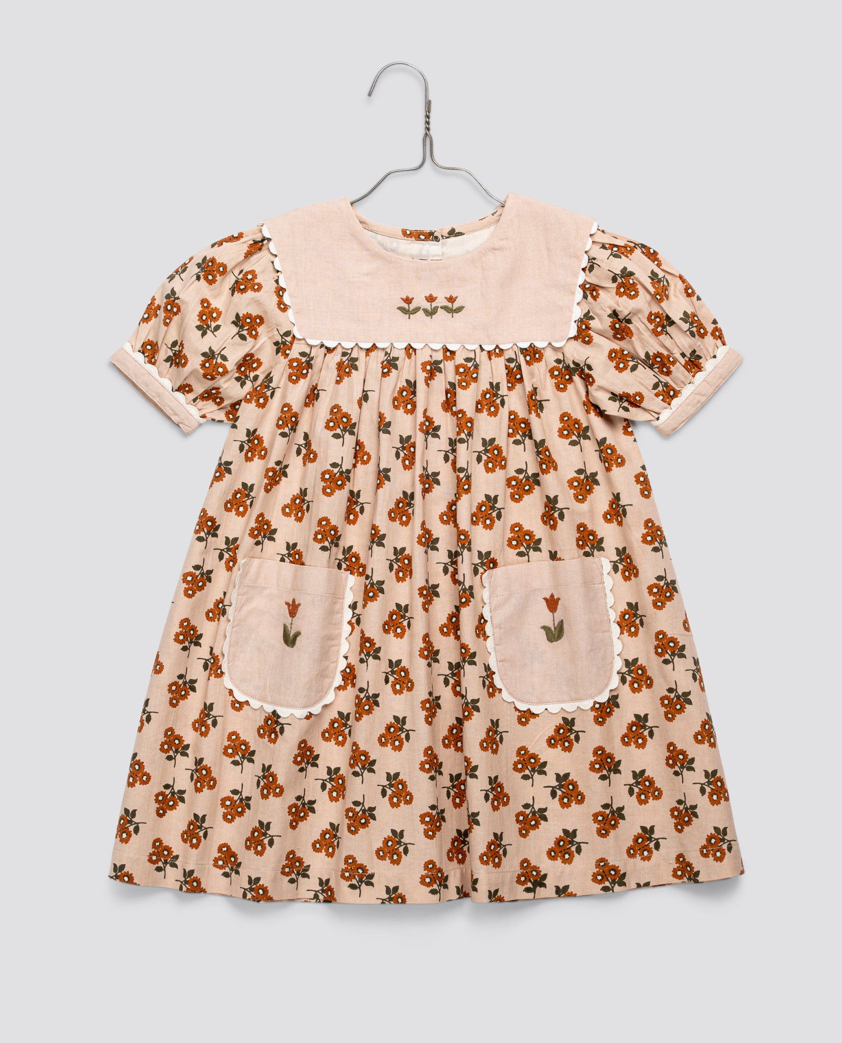 Vintage style girls dress in organic cotton with marigold floral pattern and embroidered details, featuring puff sleeves and patch pockets in a soft, natural color.
