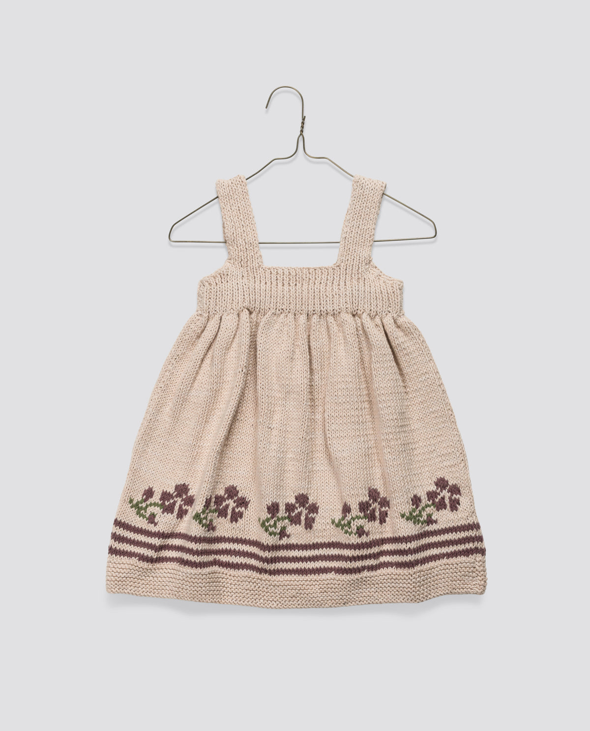 Hand-knitted beige pinafore dress for children made from soft wool, with a vintage inspired rose and stripe pattern on the hem, sustainably made for ethical kid's clothing.