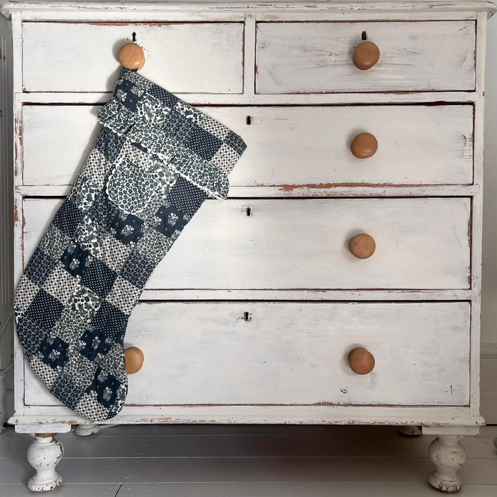 Quilted blue floral stocking with floral frill and pocket . Photographed hanging on a chest of drawers