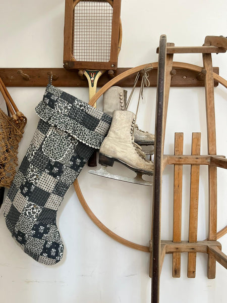 Quilted blue floral stocking with floral frill and pocket . Photographed hanging on a wooden rack with sledge and ice skates.