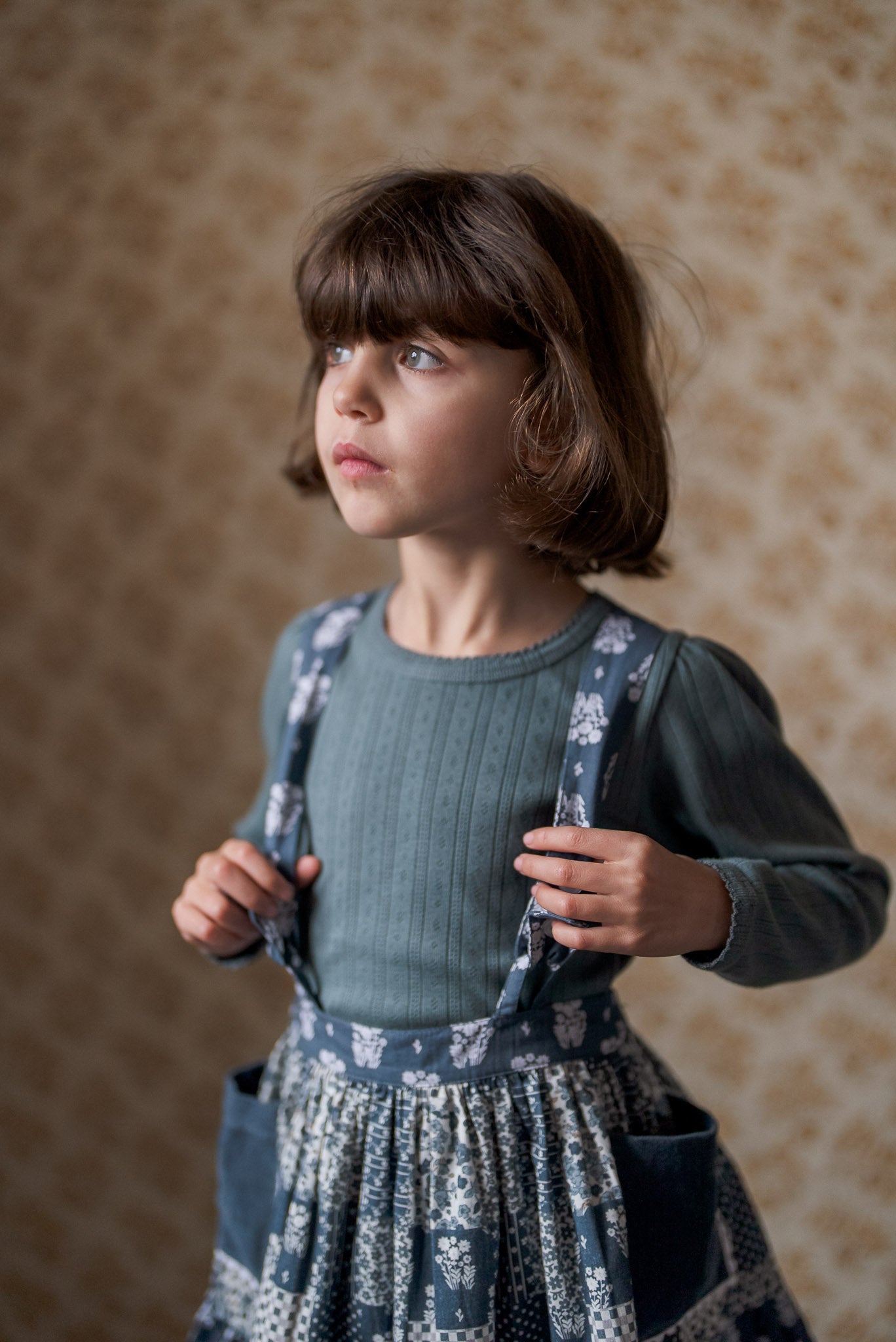 Young girl wearing a navy blue vintage style cotton dress with floral patchwork and a slate-colored pointelle cotton top, showcasing sustainable, organic children's clothing.