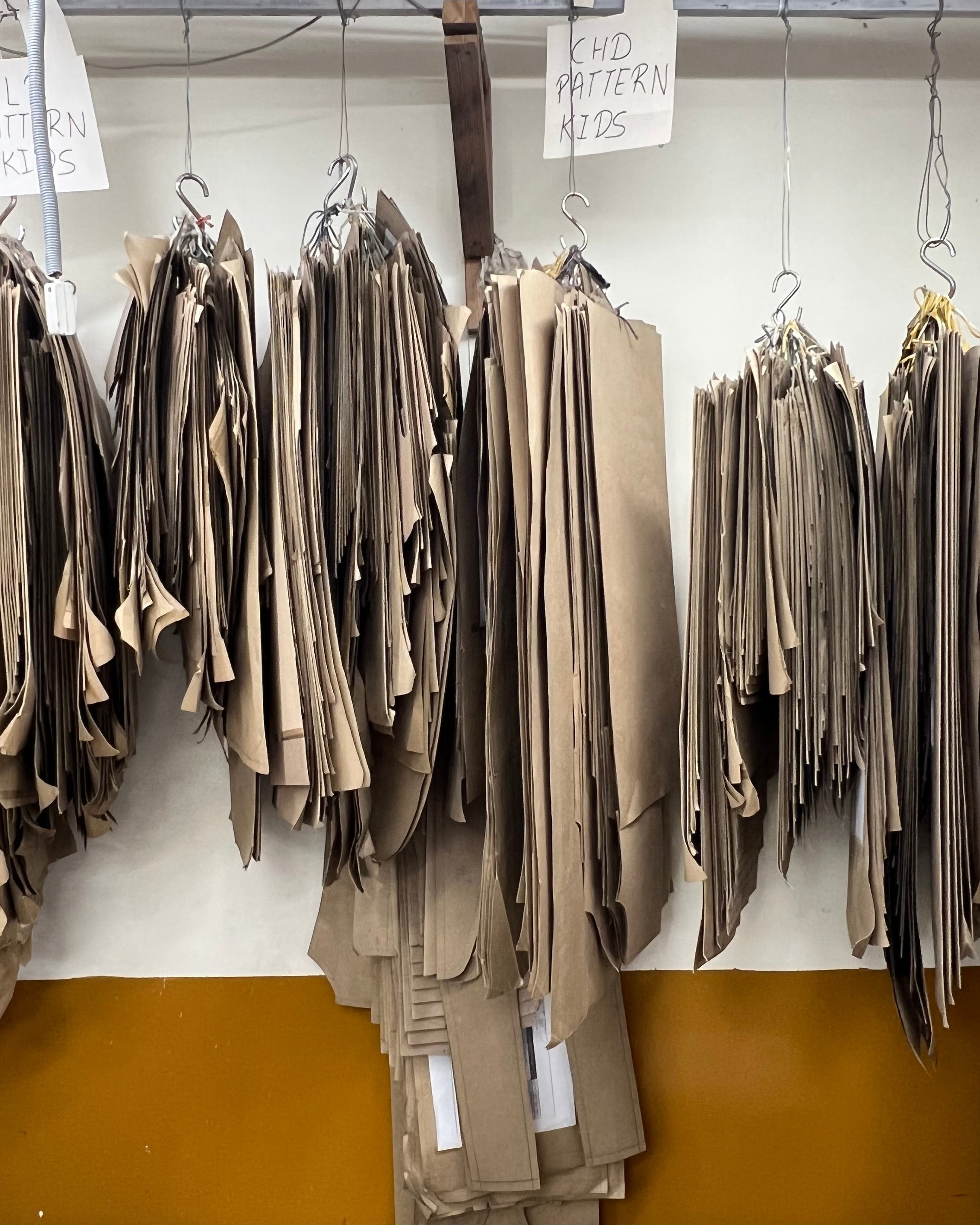 Hangers with beige pants on a rack against a white wall.