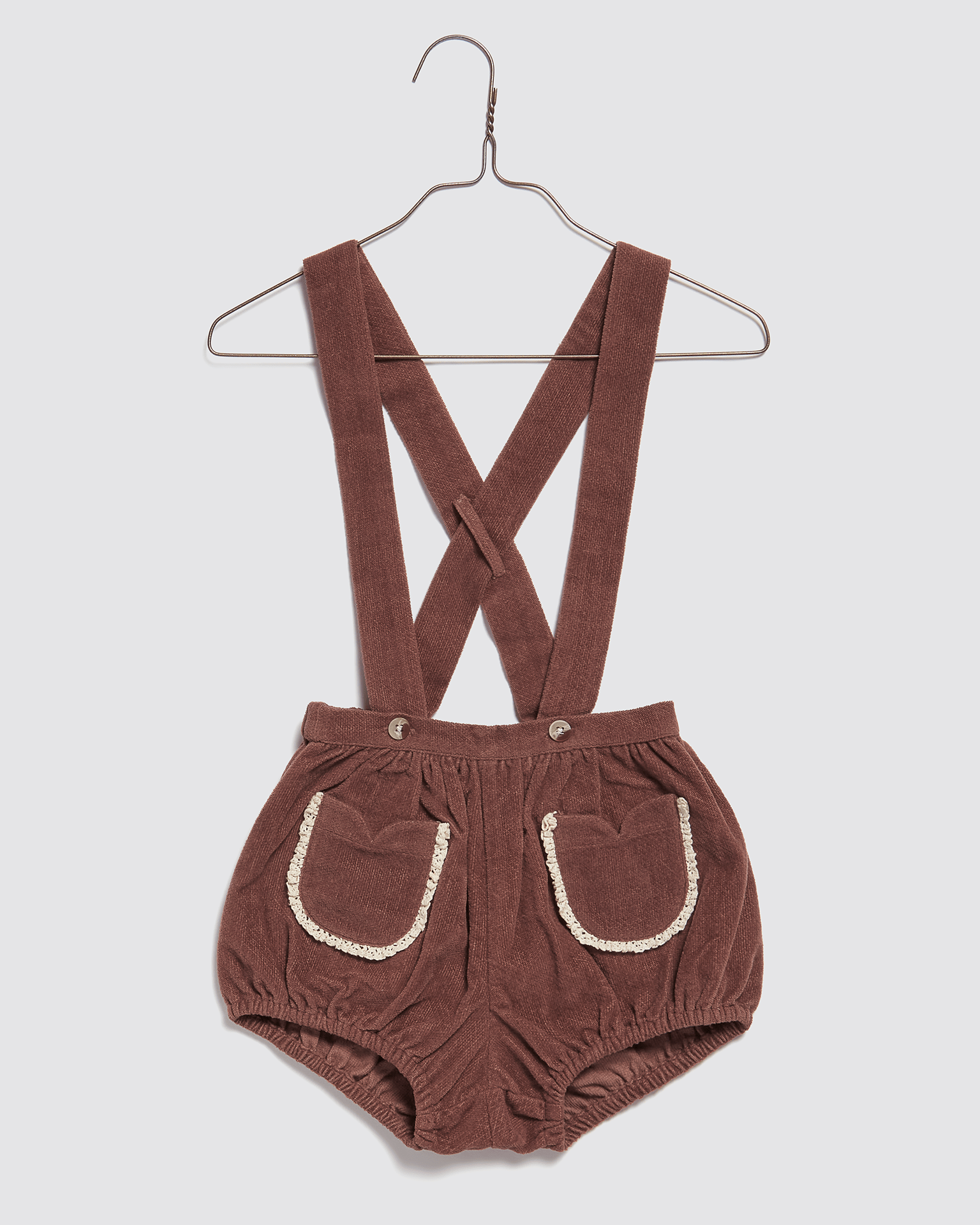 Brown velvet romper with cross-back straps and front pockets trimmed with natural-colored lace, made from organic cotton for toddlers and babies in a vintage style.